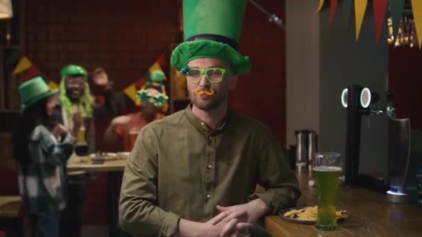 セントパトリックのお祝いの日の間にアイルランドのバーでカメラのために偽の口ひげと面白いメガネを身に着けている白人男性の中型肖像画 — ストック動画