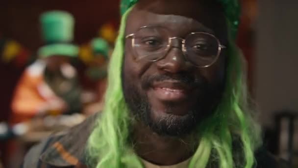 緑色のウィッグで陽気なアフリカ系アメリカ人の男を踊り カメラのために微笑み 屋内でアイルランドのスタントパトリックの日を祝うのクローズアップ肖像画 — ストック動画