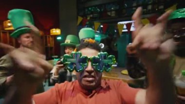 Büyük, komik yonca gözlüklü bir adamın, arkadaşlarıyla barda Aziz Patrick Günü 'nü kutlarken çekilen görüntüler.