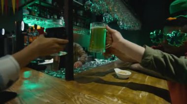 Barda oturup milli İrlanda bayramını kutladıktan sonra yeşil bardakta kadeh kaldıran müşteriler.