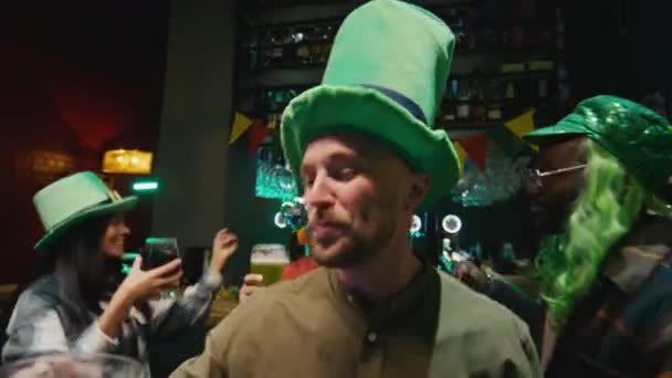 サンパトリックデーを祝うパブの仲間の友人と一緒にビールのパイントで踊る大規模な緑のレプリカンのひげの男のPov — ストック動画