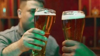Akşam barda kadeh tokuşturup bardakları tokuşturduktan sonra, Melez Adam 'ın tanınmayan arkadaşıyla bira bardağıyla tezahürat yapmasına yakın çekim.
