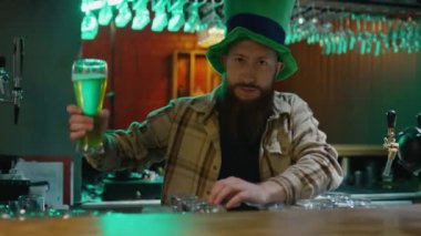Beyaz sakallı adamın orta boy portresi. Büyük yeşil cüce şapkalı. Barda yeşil bira servisi yapıyor ve Aziz Patrick Günü 'nde kameraya bakıyor.