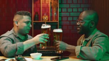 Afrika kökenli Amerikalı ve melez erkek arkadaşlarının barın önünde oturup kadeh tokuşturup kadeh tokuşturarak kadeh tokuşturuşlarının orta boy görüntüleri.