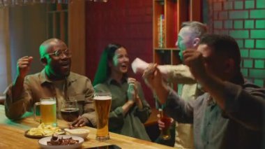 Dört farklı erkek ve kadın arkadaşından oluşan orta boy göğüs. Spor karşılaşmasında zaferi kutlayan takımlar ve barda cızırdayan bira bardakları.