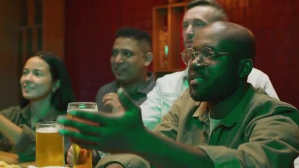 在现代酒吧里 各色人等的男男女女坐在吧台边 一边喝着啤酒一边热切地谈论着看电视的过程 — 图库视频影像