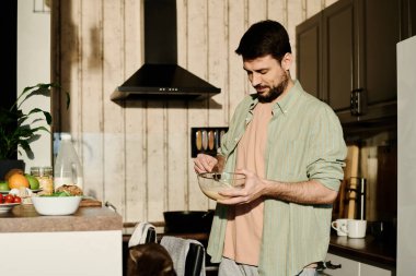 Tişörtlü adam mutfak tezgahına dayanıyor ve çiğ yumurtayı taze sütle çırpıyor. Sabahları kendi kendine kahvaltı hazırlıyor.