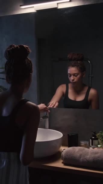 Pionowe Tylne Ujęcie Młodej Afroamerykanki Myjącej Twarz Wodą Przed Lustrem — Wideo stockowe