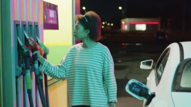 Afrika kökenli Amerikalı genç bir kadının benzin deposunu gece doldurup arabaya binerken orta ölçekli görüntüleri.