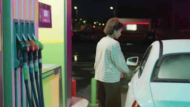 夜に車のガソリンタンクを給油するためにコラムで車から降りる若いアフリカ系アメリカ人女性のサイドフルメディア映像 — ストック動画