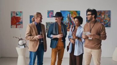 Sergi açılışında tabloların önünde duran, şampanya bardakları tutan, sohbet eden ve kameraya bakıp gülümseyen çağdaş sanat galerisi ekibinin orta boy portresi.