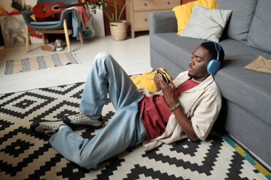 Akıllı telefonlu Afro-Amerikalı adam oyun alanına bağlı, boş zamanlarında kanepede dinlenirken video oyunu oynuyor.