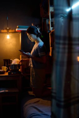 Cep telefonlu genç bir kadın mikrofonda elektrikli ocağın başında dikilip yemek pişirirken internetten video mu izliyor yoksa mesajlaşıyor mu?