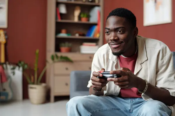 笑顔のアフリカ系アメリカ人の男は コントローラーのボタンを押し ビデオゲームをプレイしながらコンピュータやテレビの画面を見ています — ストック写真