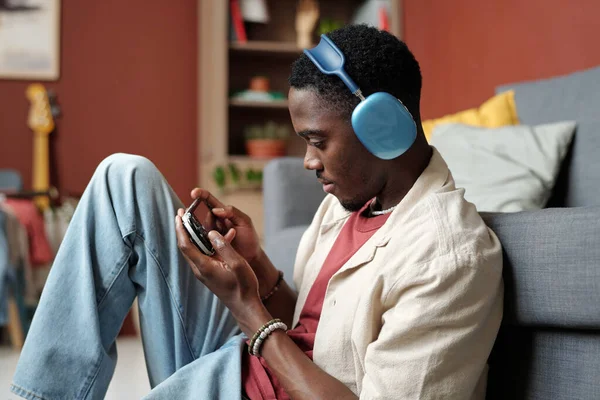 家庭環境でのレジャーでビデオゲームをプレイしながら ゲームパッドを見ながらスマートフォンに接続された若い男性ゲーマー — ストック写真