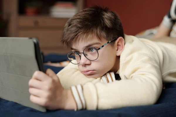 Gözlüklü Sarışın Çocuk Kameranın Önünde Yatağında Dinlenirken Tablet Ekrana Bakıyor — Stok fotoğraf