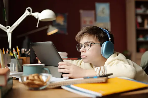 眼鏡やヘッドフォンの真剣な学校児童がタブレットの画面を見ながら自宅の課題を遂行したり オンラインレッスンを見ている — ストック写真