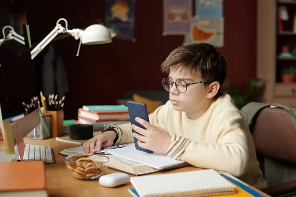 オープンテキストブックの前に机に座り 宿題をしたり 主題に関するオンライン情報を調べたりする真剣な若い少年 — ストック写真