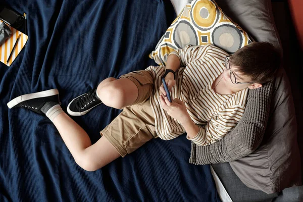 Bovenaanzicht Van Schooljongen Met Smartphone Zittend Bed Tegen Kussens Communicerend — Stockfoto