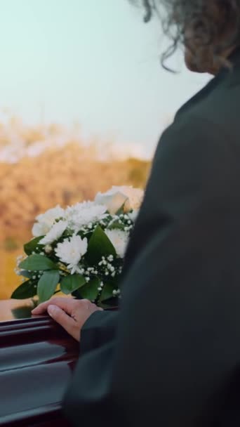 在户外丧礼上 一个无法辨认的女人把手放在白色花朵附近的木棺材盖上的垂直弧形镜头 — 图库视频影像
