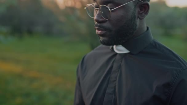 アフリカ系アメリカ人の司祭をメガネで閉じ 屋外埋葬式の祈祷書から葬儀サービスを読みました — ストック動画