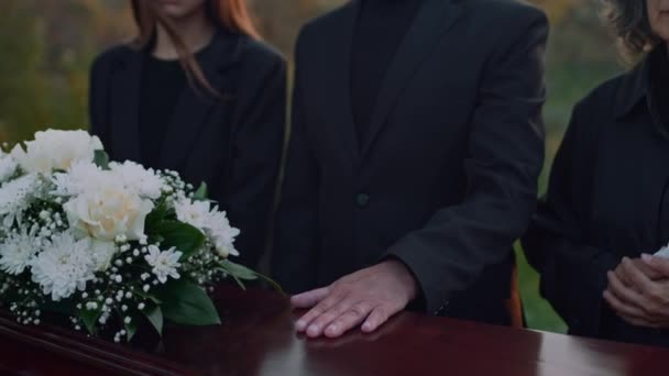 墓地での記念礼拝中に白い花で棺のふたを手に入れたサングラスの上級白人男性の映像に傾いた — ストック動画
