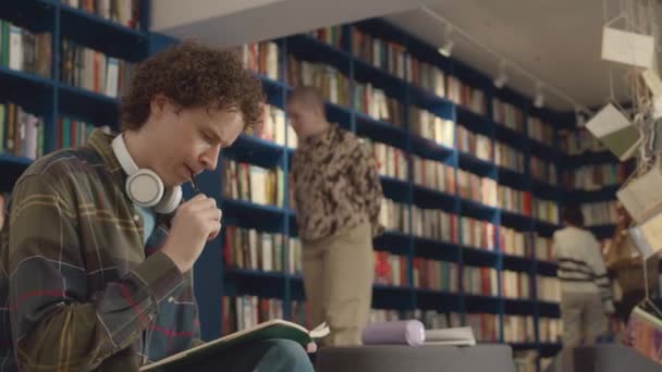 도서관에 머리를 코카서스 대학생의 노트북에 에세이 헤드폰에 배경에 사람들 — 비디오