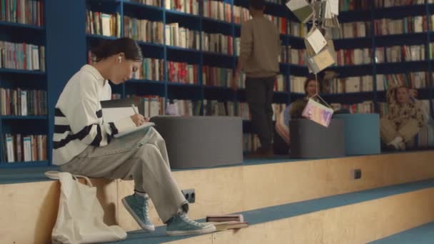스트라이프 점퍼에 아시아 학생의 바지와 도서관에 벤치에 교과서와 노트북에 그리고 — 비디오