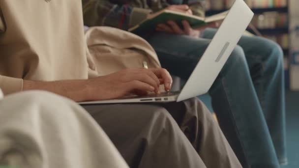 坐在大学图书馆的阿拉伯年轻人的特写镜头 在写研究生论文的时候在笔记本电脑上打字 与正在看屏幕和做笔记的白人朋友讨论任务 — 图库视频影像