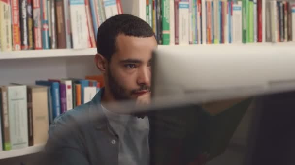 集中注意力的中东年轻男生坐在图书馆的台式计算机前 一边看屏幕 一边在键盘上思考和打字 一边做论文的中等特写镜头 — 图库视频影像