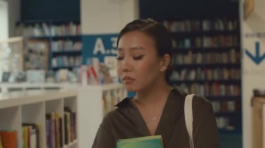 Üniversite sınavlarına hazırlanmak için kitap aldıktan sonra kütüphaneden ayrılan yüzü endişeli ve stresli güzel bir Asyalı kadının yakın çekim görüntüsü.