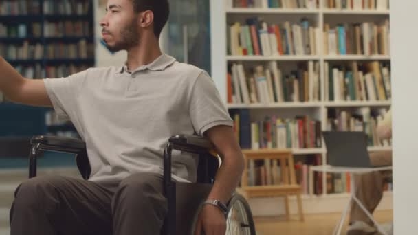 장애를 남자의 기울이는 도서관 주위에 휠체어 선반에 디스플레이에 제목을보고 공부를위한 — 비디오
