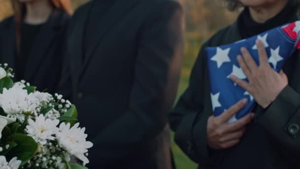 アウトドアの葬儀で棺の近くに立っているアメリカの国旗を抱き悲しんでいるコーカサス高齢女性の側傾きのクローズアップ — ストック動画