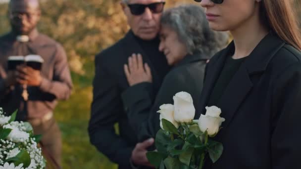 屋外の葬儀の儀式で手で白いバラと木製のカスケットを見ている白い女性の側傾きのクローズアップ — ストック動画