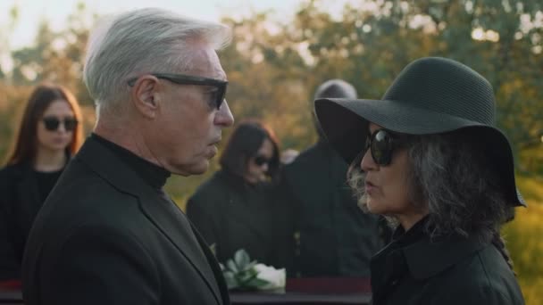 シニアの両親がお互いに話し合い 屋外の葬儀で妻を慰める男の横の傾きの映像 — ストック動画