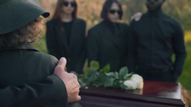 屋外の葬儀の際に彼女を慰める女性の肩に手を置く匿名の人物の後ろのクローズアップ — ストック動画