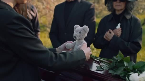 子供のための屋外の葬儀の間に棺のふたにテディベアを置く認識できない女性のサイドミッドセクション映像 — ストック動画