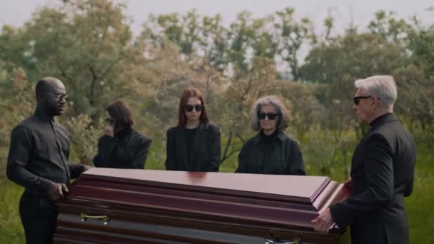 男性の多様なパレベーターのフルメディアサイド映像はゆっくりと木製のカスケット蓋を閉じ 墓地での葬儀の儀式で棺を取ります — ストック動画