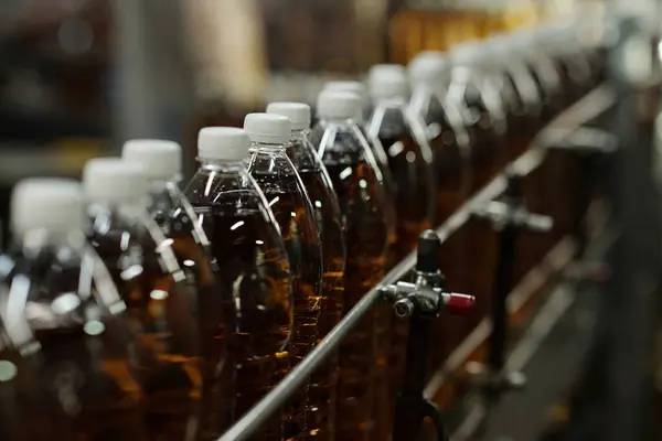 Row of packed plastic bottles containing soda with white caps moving along assembly line or belt conveyor in large factory