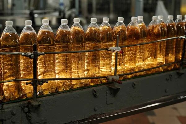 Part of long line of capped bottles with fizzy soda or lemonade moving along automated robotic conveyor belt at modern beverage plant