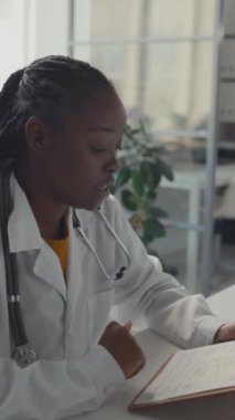 Hastanedeki genç Afrikalı Amerikalı kadın hekimin durumu ve şikayetleri hakkında soru sorduğu ve klinik tavsiyelerde bulunduğu orta boy dikey bir fotoğraf.