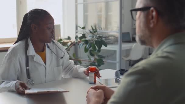 실험실 코트에 아프리카계 미국인 여성의 진료소에서 책상에 스테로스코프 성숙한 코카서스 — 비디오