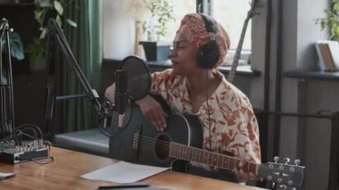 Gitarlı kadın Afrikalı Amerikalı müzisyenin stüdyoda podcast şovunda mikrofona konuşmasının yan görüntüleri.