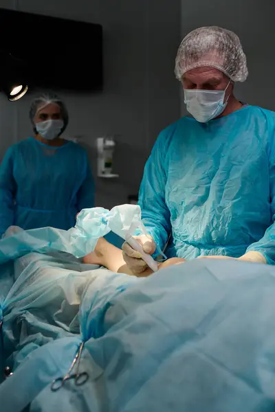 外科手術中に患者の膝によってプローブを保持する保護マスク 手袋および医療スクラブの経験豊富な男性外科医 — ストック写真