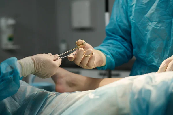 外科手术期间 辅助人员将钢制无菌钳传给外科医生的手套手 而不是餐巾纸覆盖的病人 — 图库照片