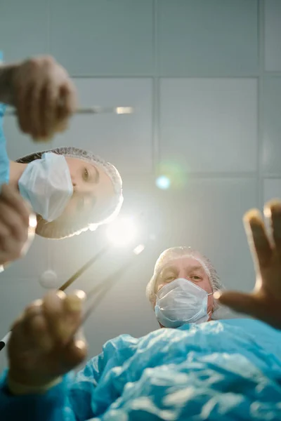 成熟した外科医の低角度と医療スクラブ マスク 手袋のアシスタントは 患者の上に曲がり 操作を行います — ストック写真