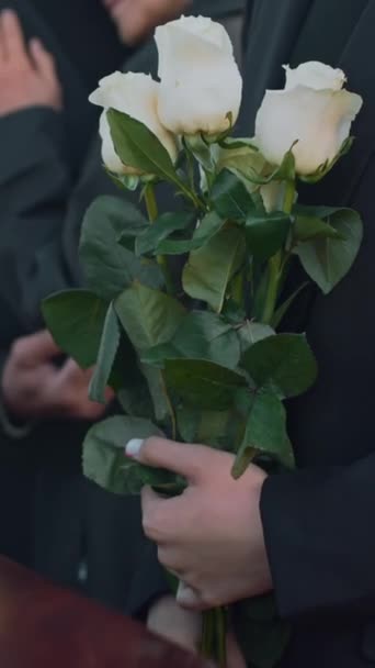木製の棺で立って 屋外の葬儀で白いバラを手に持っている 認識できない女性の横の垂直に作られた映像 — ストック動画