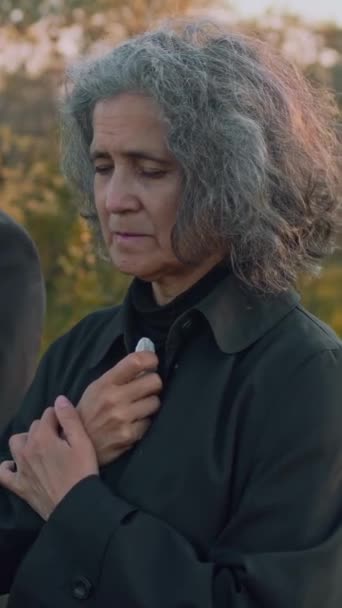 墓地での記念式典中に祈り泣いている白人上級女性の横の垂直映像 — ストック動画