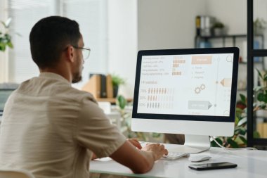 Genç İK yöneticisi bilgisayar ekranında istatistik verilerine bakıyor ve Openspace ofisinde masa başında otururken klavyede daktilo kullanıyor