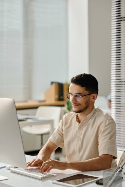 Genç Müslüman erkek işçi bilgisayar klavyesinde yazı yazıyor ve elektronik belgeye veri girerken ekrana bakıyor
